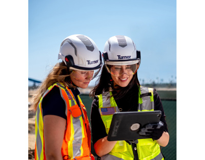 two women in safety vest and hard hats looking down at an ipad